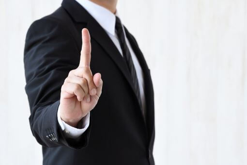 人差し指をたてるスーツの男性